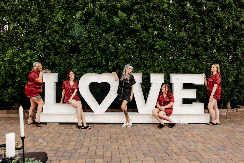 lgbtqia gothic wedding in phoenix arizona at the venue at chileens in black wedding dress with bride and bridesmaids in front of Love sign