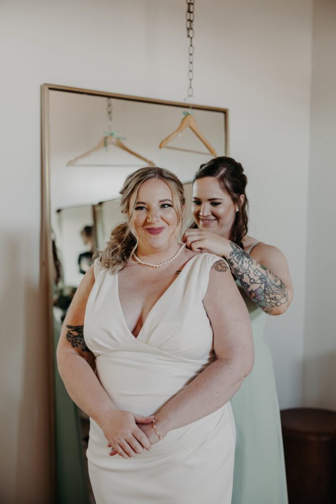 plus size bride wearing vneck crepe sheath wedding dress getting necklace put on