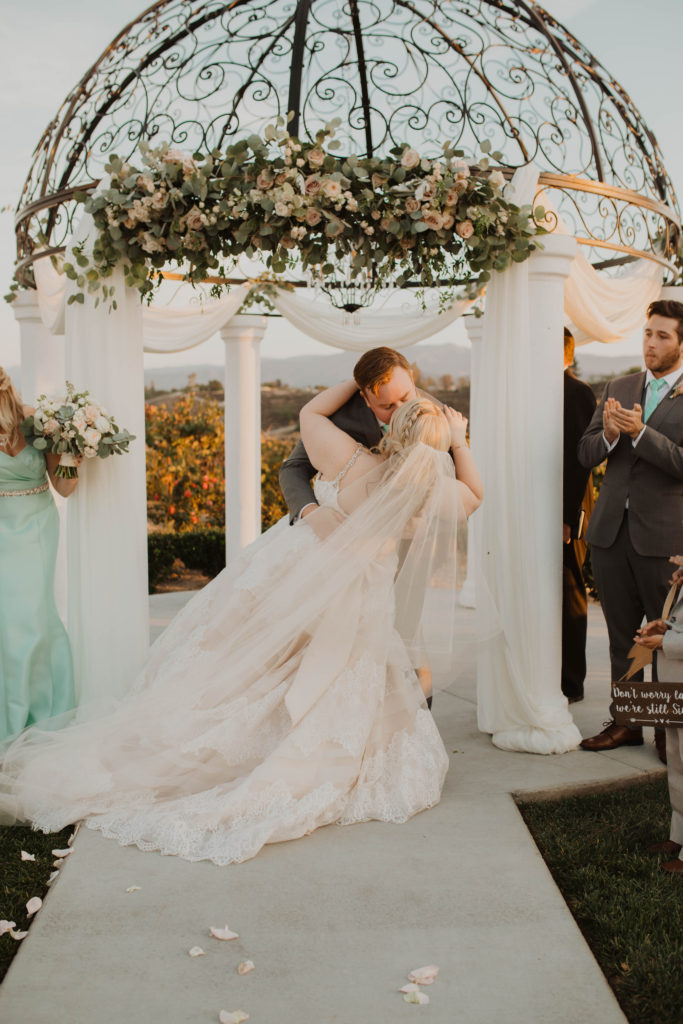 first kiss bride and groom under wedding arch