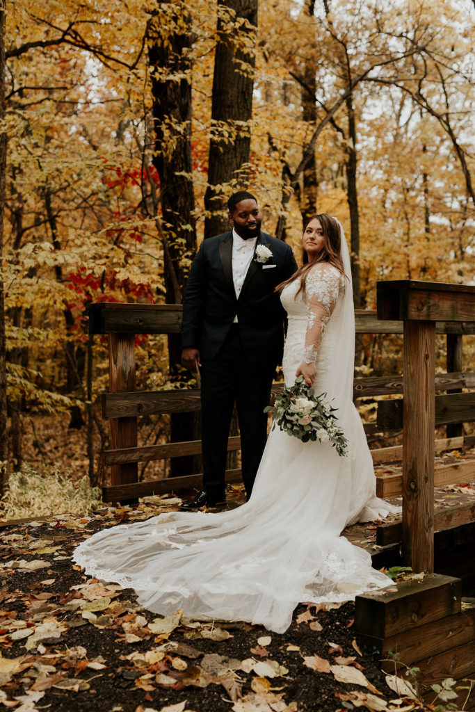 newlyweds in woods on bridge with cathedral veil