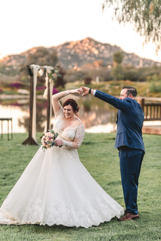 newlyweds twirling on the lawn by a lake