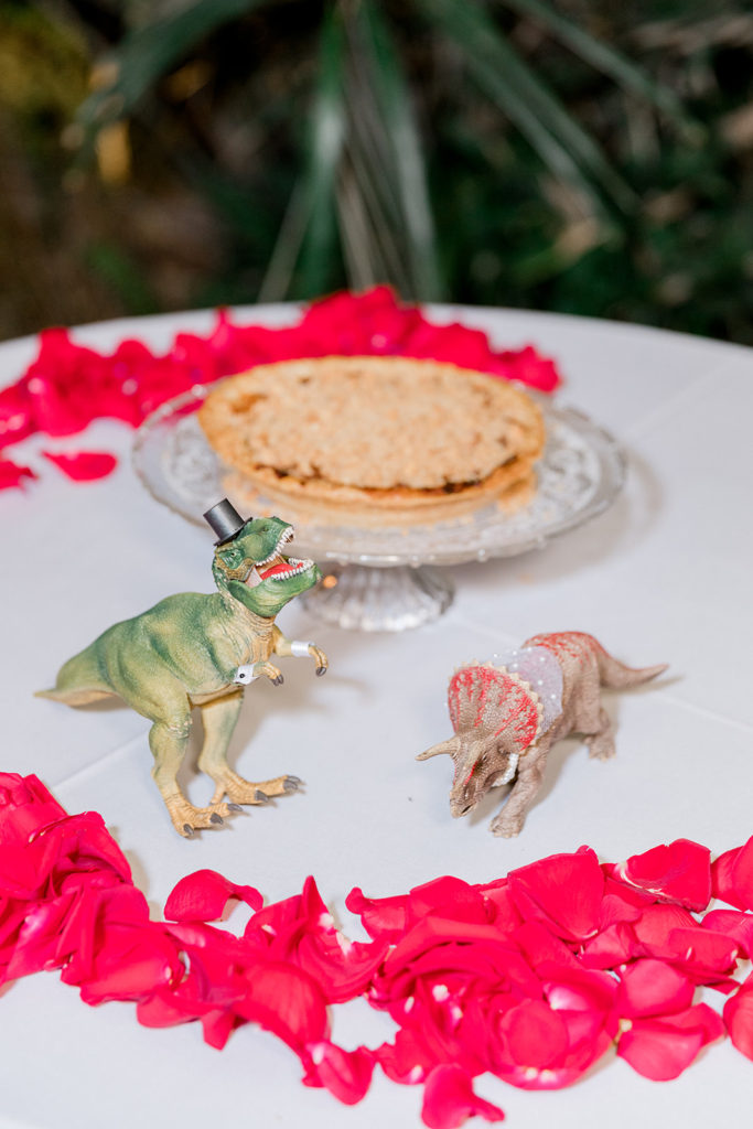 wedding dessert table with dinosaurs and red rose petals