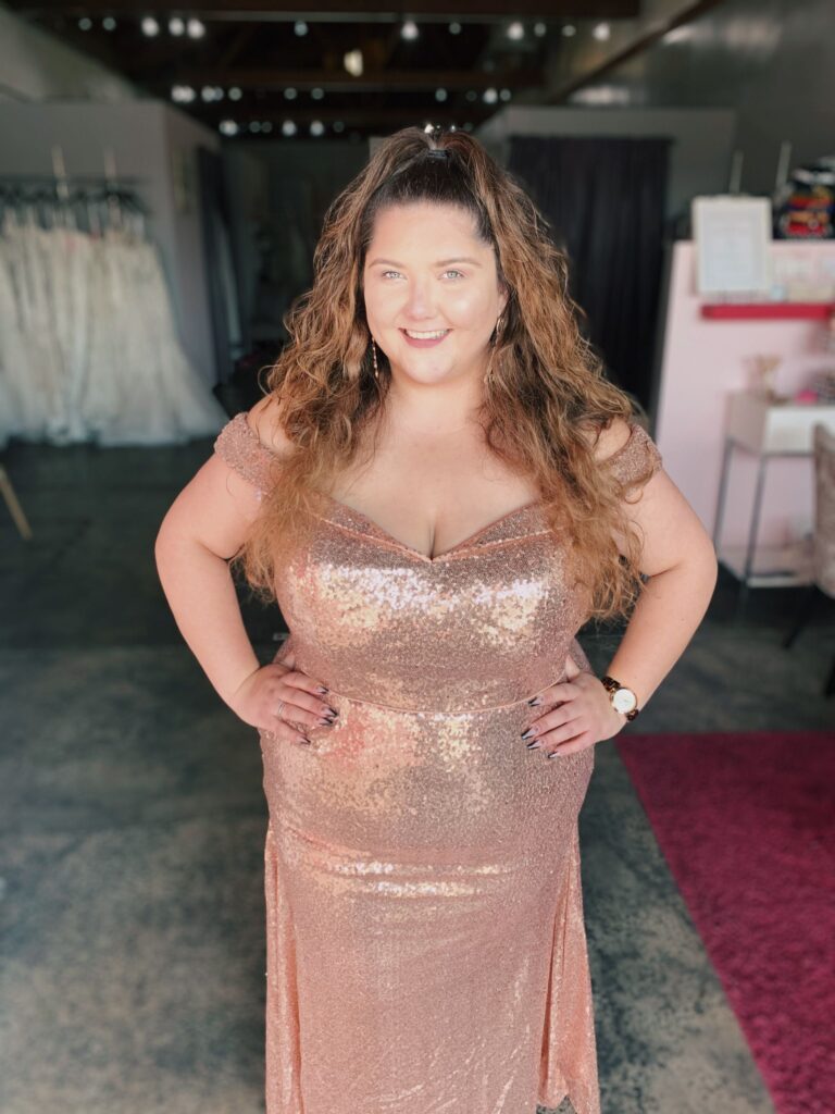 Plus size model in pretty rose gold sequin bridesmaids dress with off the shoulder sleeves and draped sides