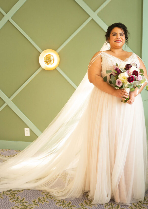 plus size bride wearing flowy wedding dress in front of green wall