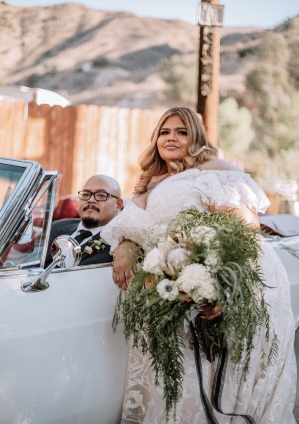 bride leaning on old car holding wedding bouquet