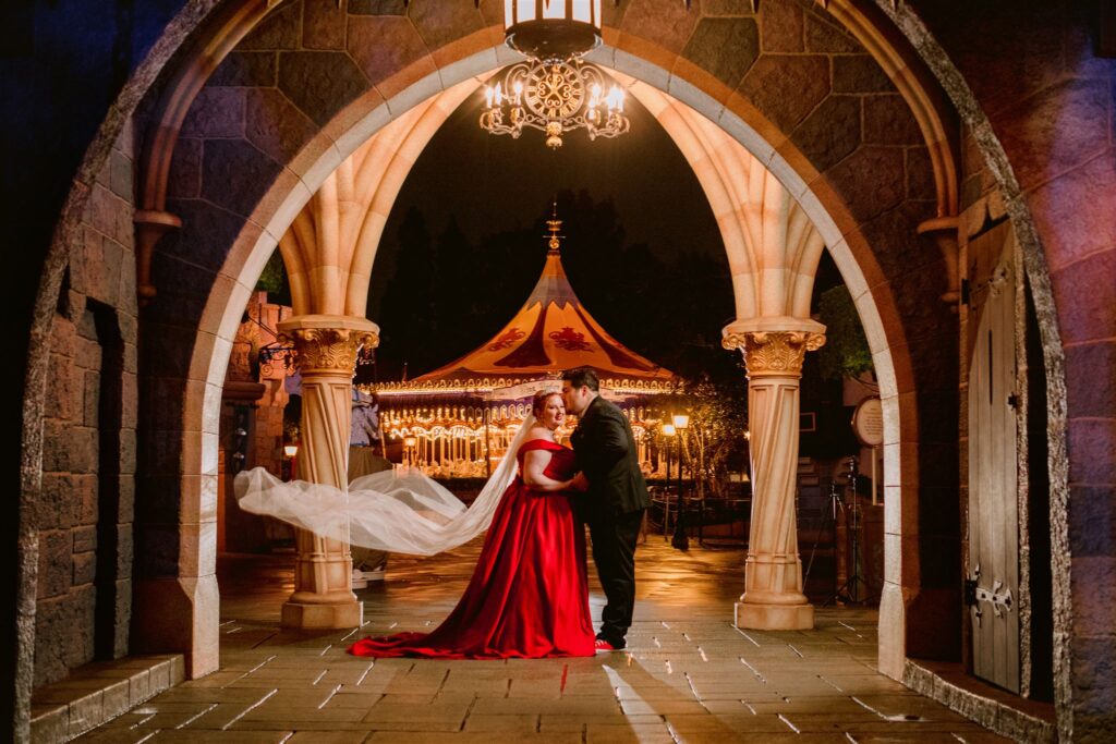 bride in red wedding dress with groom under arch at disneyland