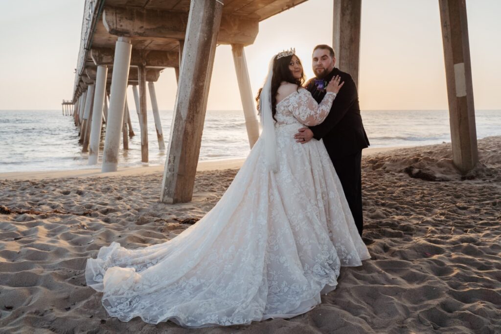 plus size bride and groom under california pier