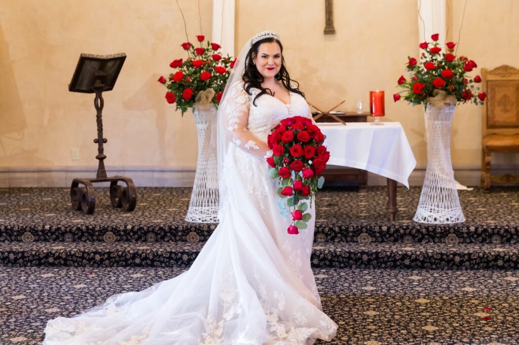 mid size bride wearing long sleeve lace wedding dress holding red rose bouquet arizona