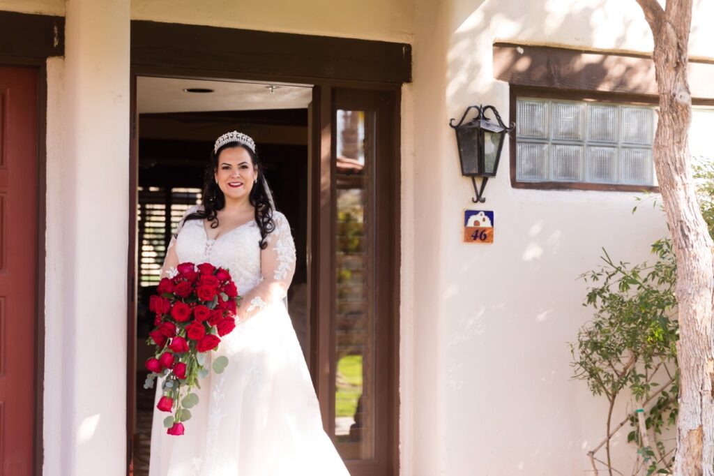 mid size bride wearing long sleeve lace wedding dress holding red rose bouquet arizona