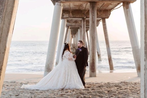 plus size bride and groom under california pier