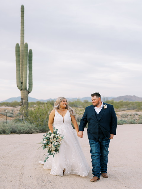 bride in lace ballgown wedding dress holding hands with groom in arizona desert