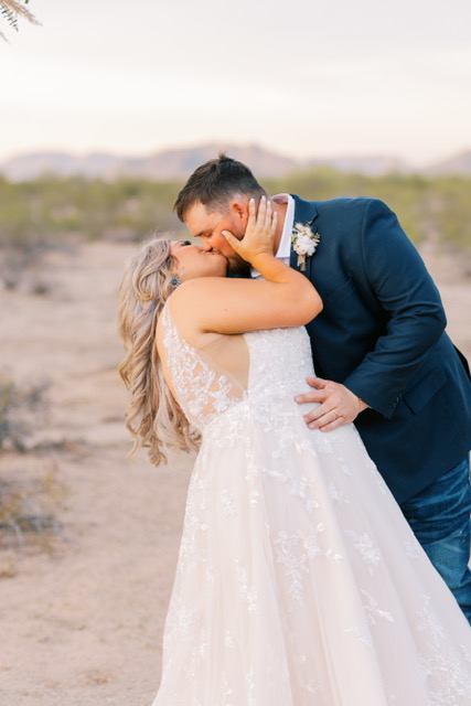 bride in lace ballgown wedding dress kissing groom in arizona desert