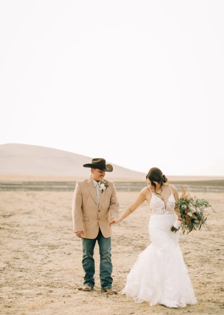 bride and groom holding hands on ranch in wedding dress california