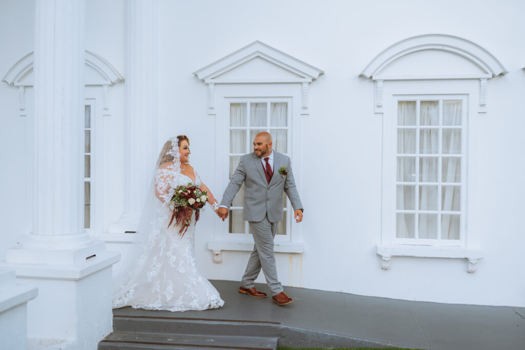 plus size bride wearing long sleeve lace fitted wedding dress with long dramatic lace train with groom in gray suit