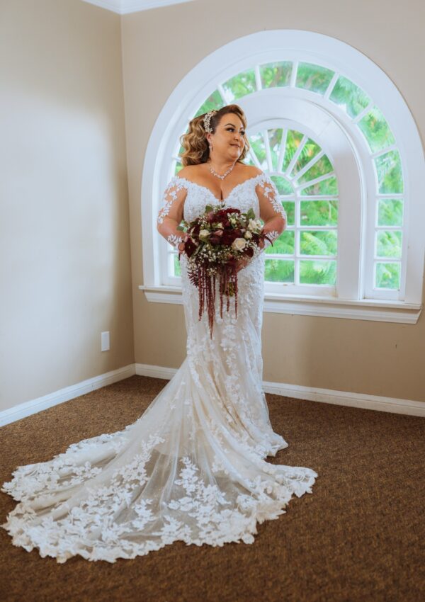 plus size bride wearing long sleeve lace fitted wedding dress with long dramatic lace train holding red bouquet