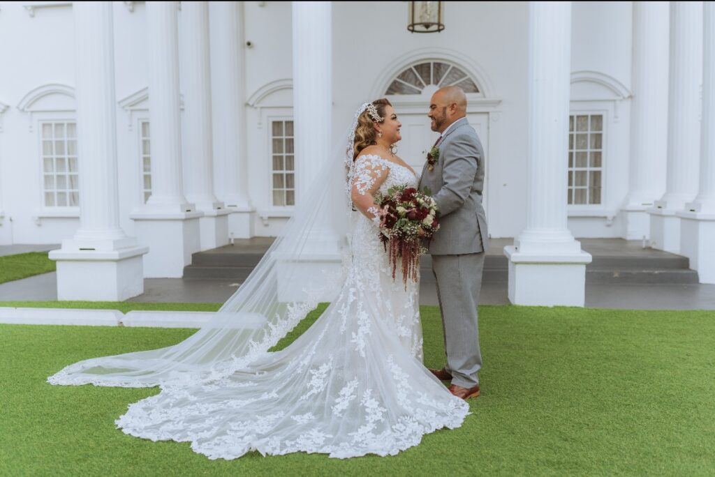 plus size bride wearing long sleeve lace fitted wedding dress with long dramatic lace train with groom in gray suit