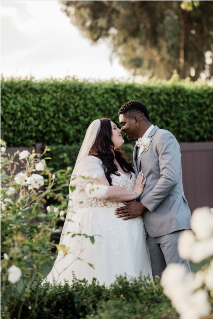 plus size bride wearing lace and tulle classic aline wedding dress holding white wedding bouquet groom in gray suit