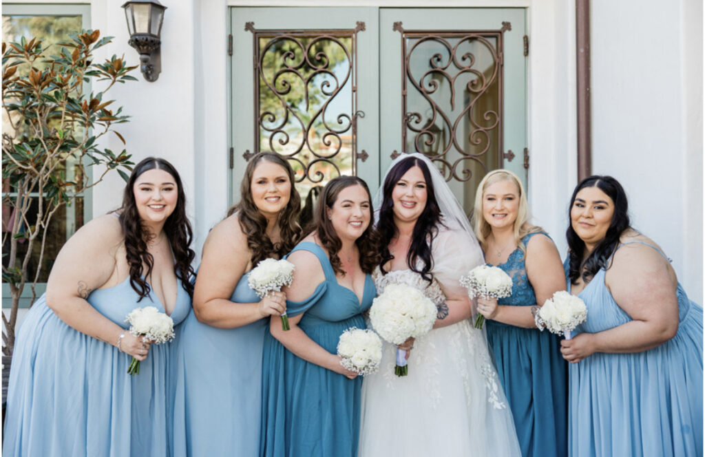 plus size bride wearing lace and tulle classic aline wedding dress holding white wedding bouquet with plus size bridemaids in blue dresses