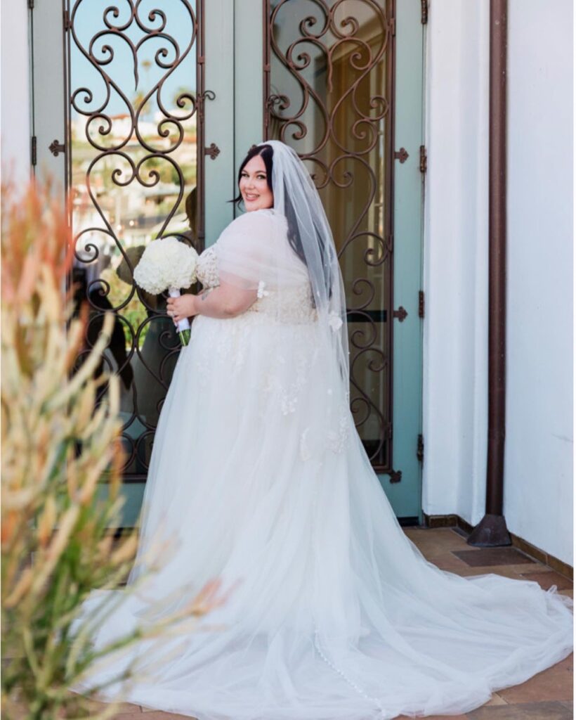 plus size bride wearing lace and tulle classic aline wedding dress holding white wedding bouquet wearing sleeves