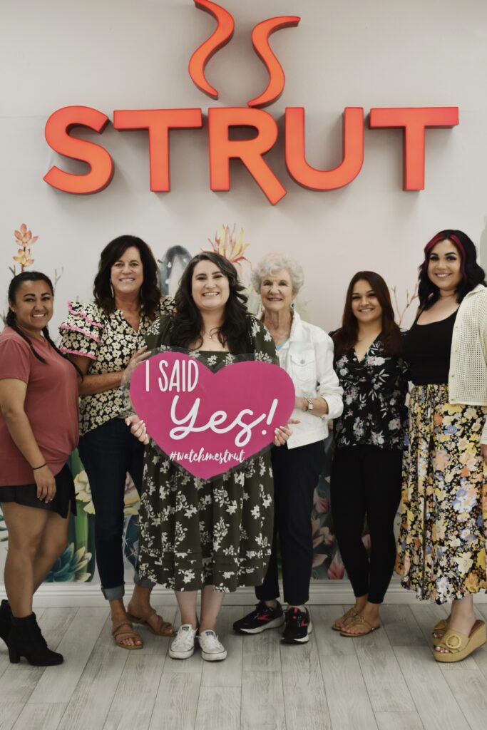 plus size bride holding i said yes sign with friends in chandler arizona bridal store