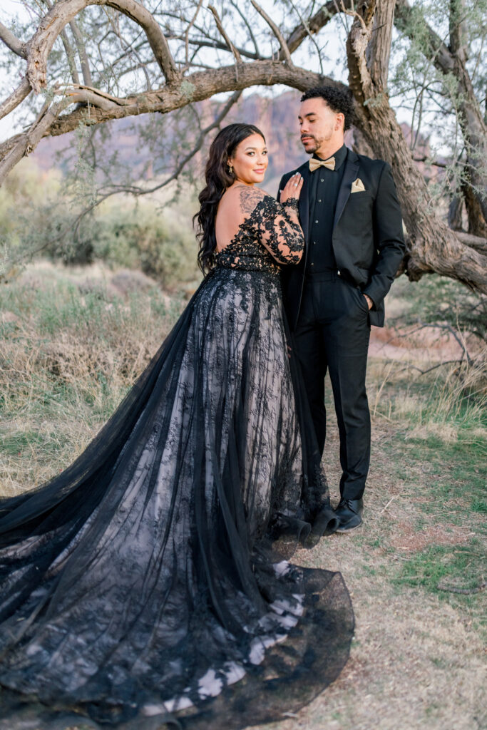 bride and groom in desert wearing long sleeve black lace ballgown wedding dress