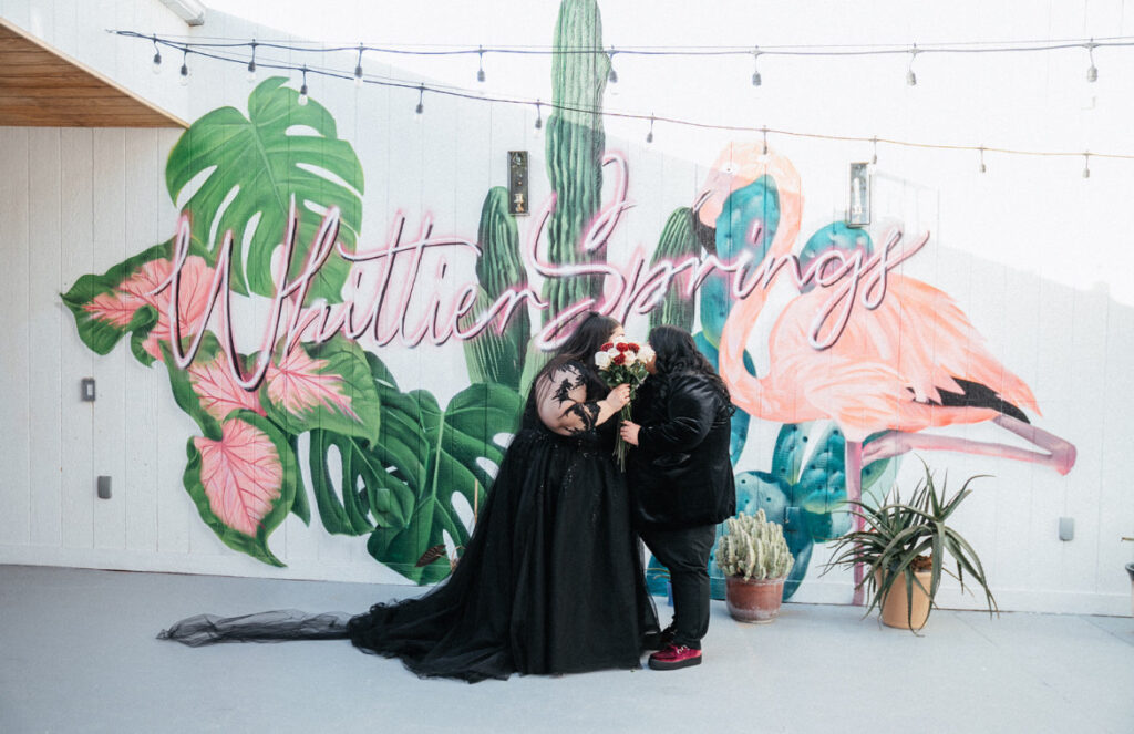 same sex couple in black wedding dress in front of whittier springs mural